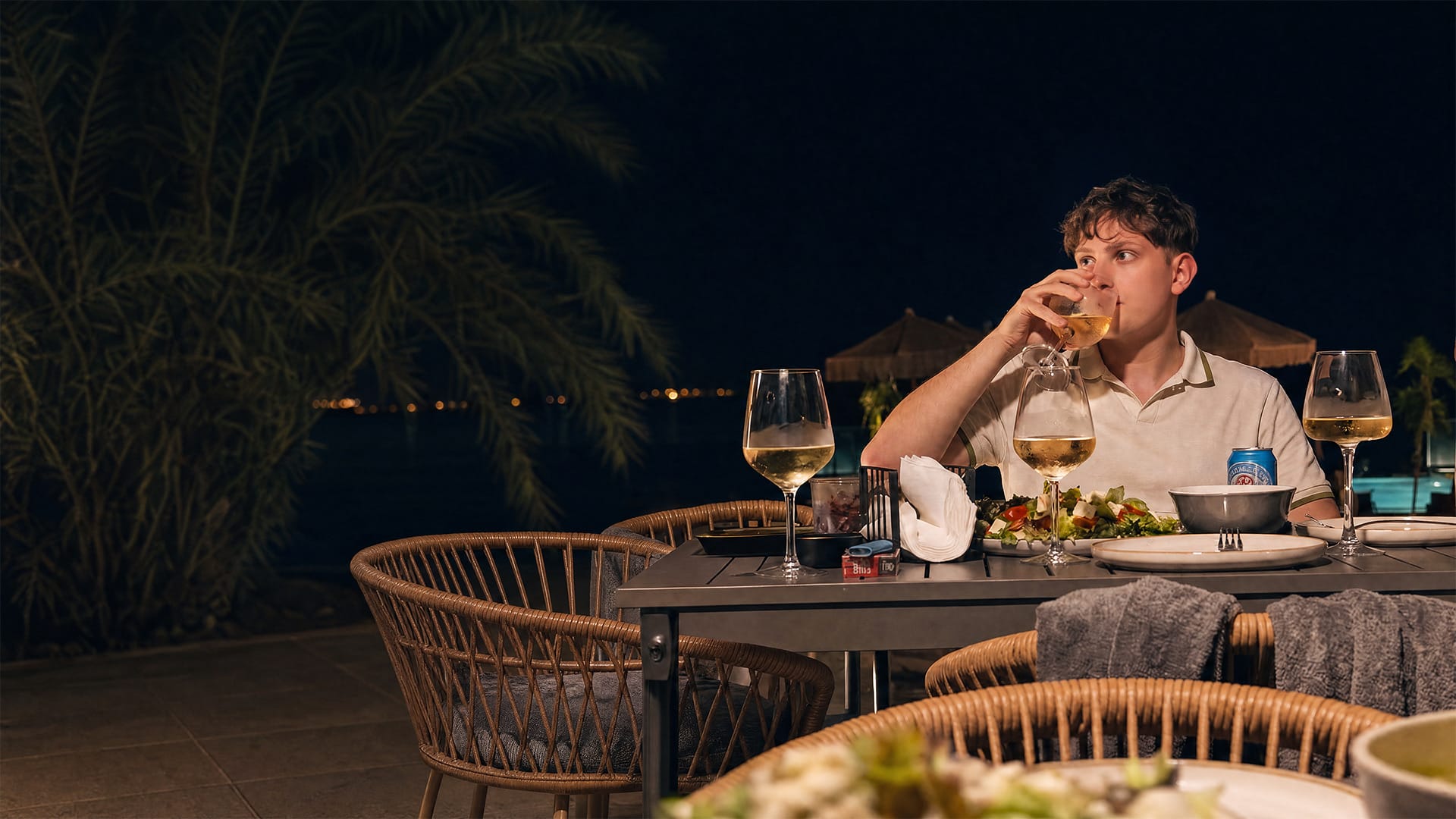 Armin Kadic trinkt abends ein Glas Wein an einem Tisch am Pool, warmes Licht